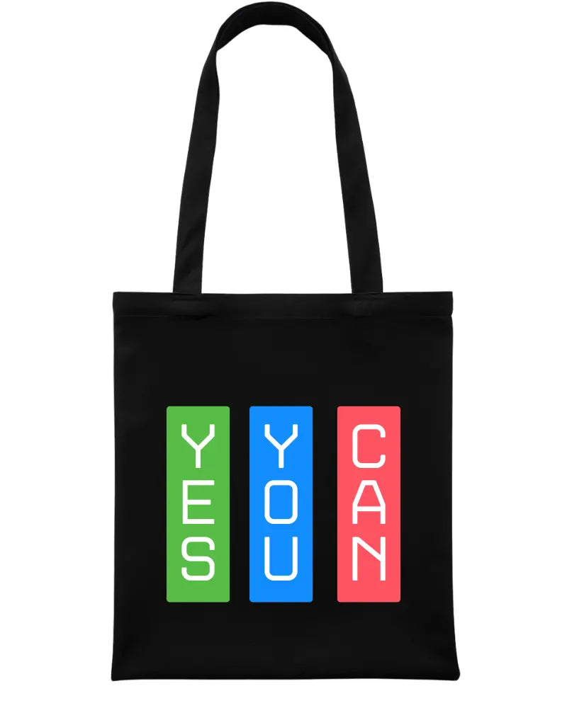 A black canvas tote bag with two shoulder straps, featuring a graphic print on the front with the words 'YES YOU CAN' stacked vertically in white text inside green, blue, and red rectangular blocks.
