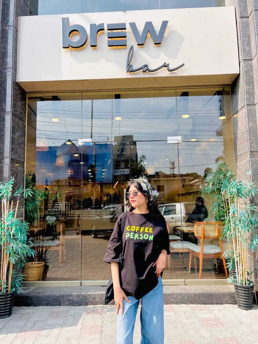 A woman wearing a black graphic t-shirt that reads 'COFFEE PERSON'