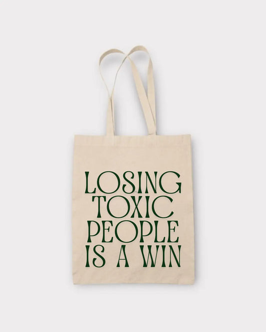 Beige tote bag with green text 'LOSING TOXIC PEOPLE IS A WIN'