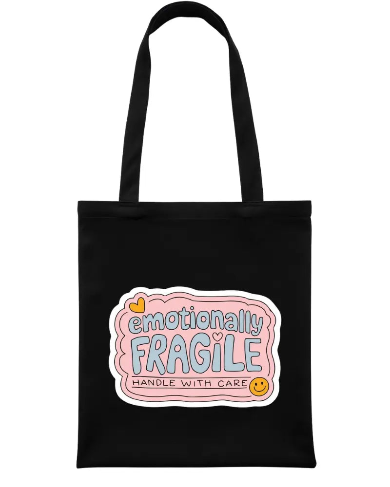 A black canvas tote bag with two shoulder straps, featuring a graphic label on the front that reads 'emotionally FRAGILE HANDLE WITH CARE' in pastel pink, blue, yellow, and orange tones.